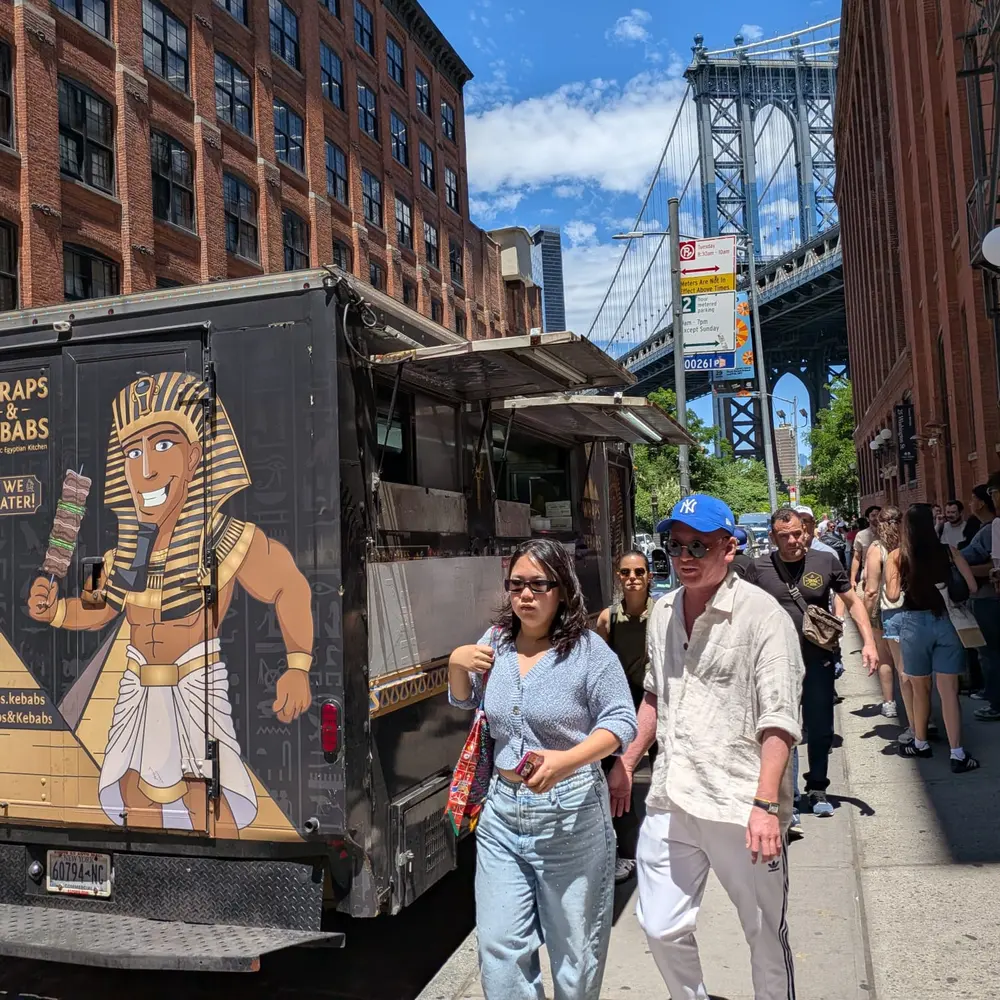 The black and gold Wraps & Kebabs truck parked in DUMBO, with the Manhattan Bridge and pedestrians behind it