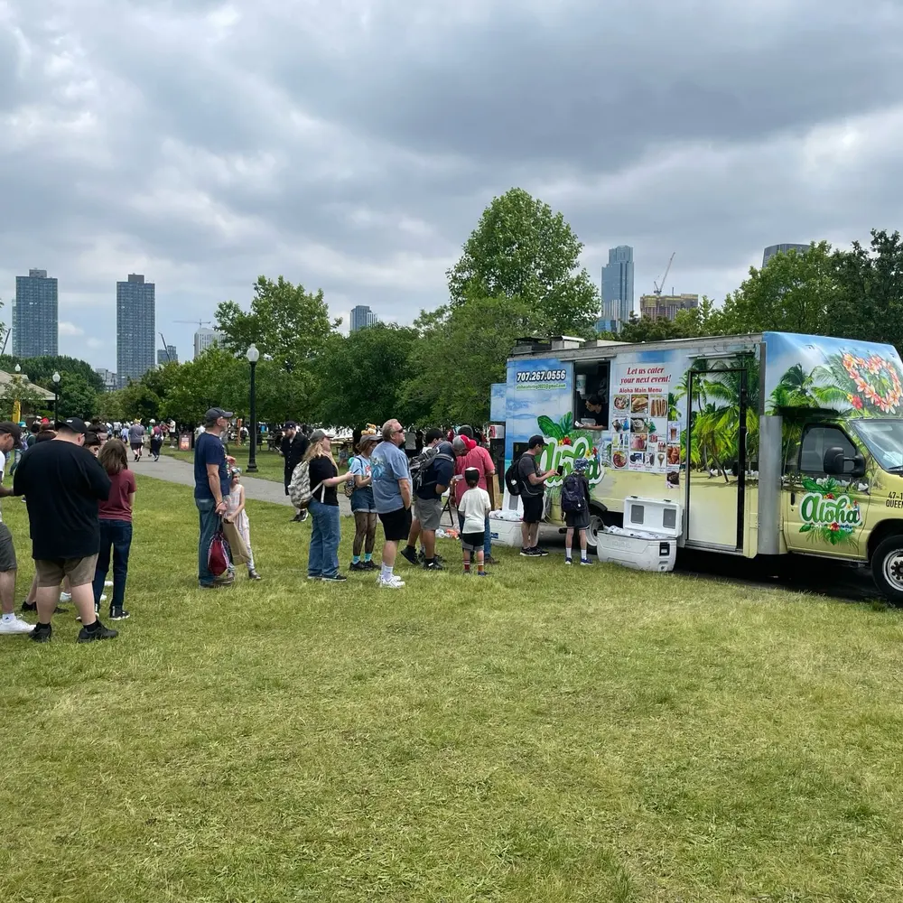 The Aloha truck's tropical mural in a city park, with a line of customers and the Queens skyline behind it