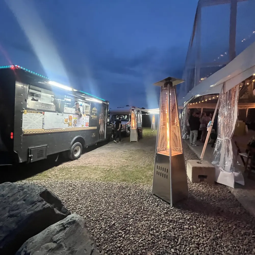 The Wraps & Kebabs truck parked beside a white tented event at dusk, patio heaters glowing on the gravel path