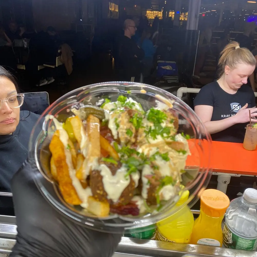 A crew member handing a finished poke bowl through the Aloha truck's window to a customer's gloved hand