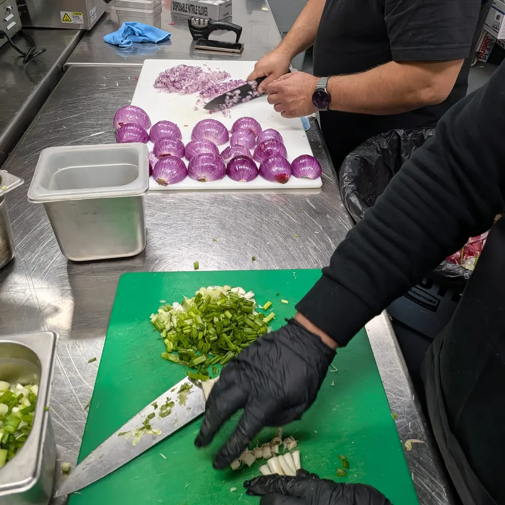 A cook in black gloves chopping scallions and red onion at the prep station