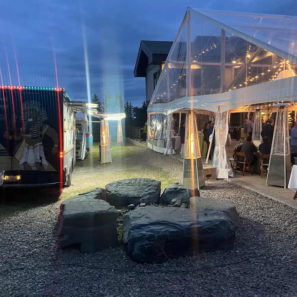 The Wraps & Kebabs truck beside a gravel path lined with patio heaters, leading to a tented event at dusk