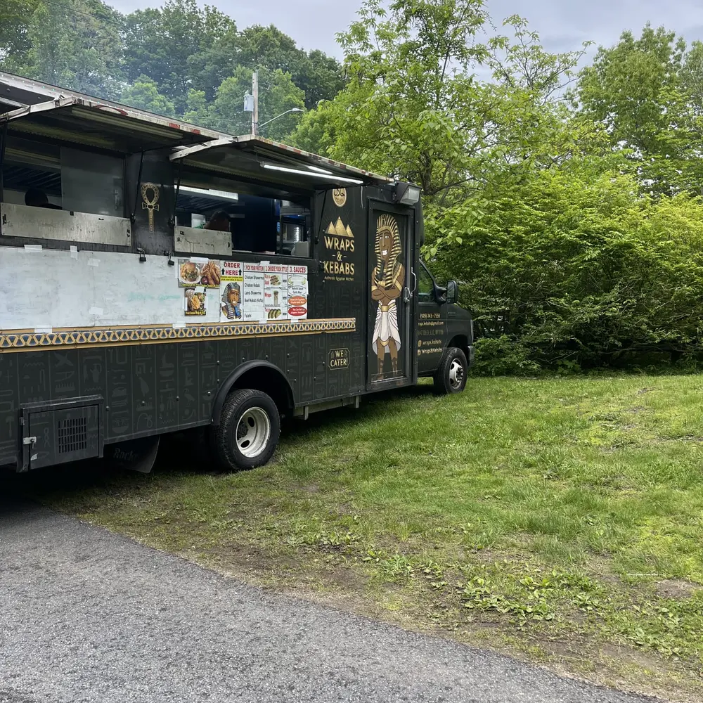 The Wraps & Kebabs truck parked at the edge of the woods beside a tented event