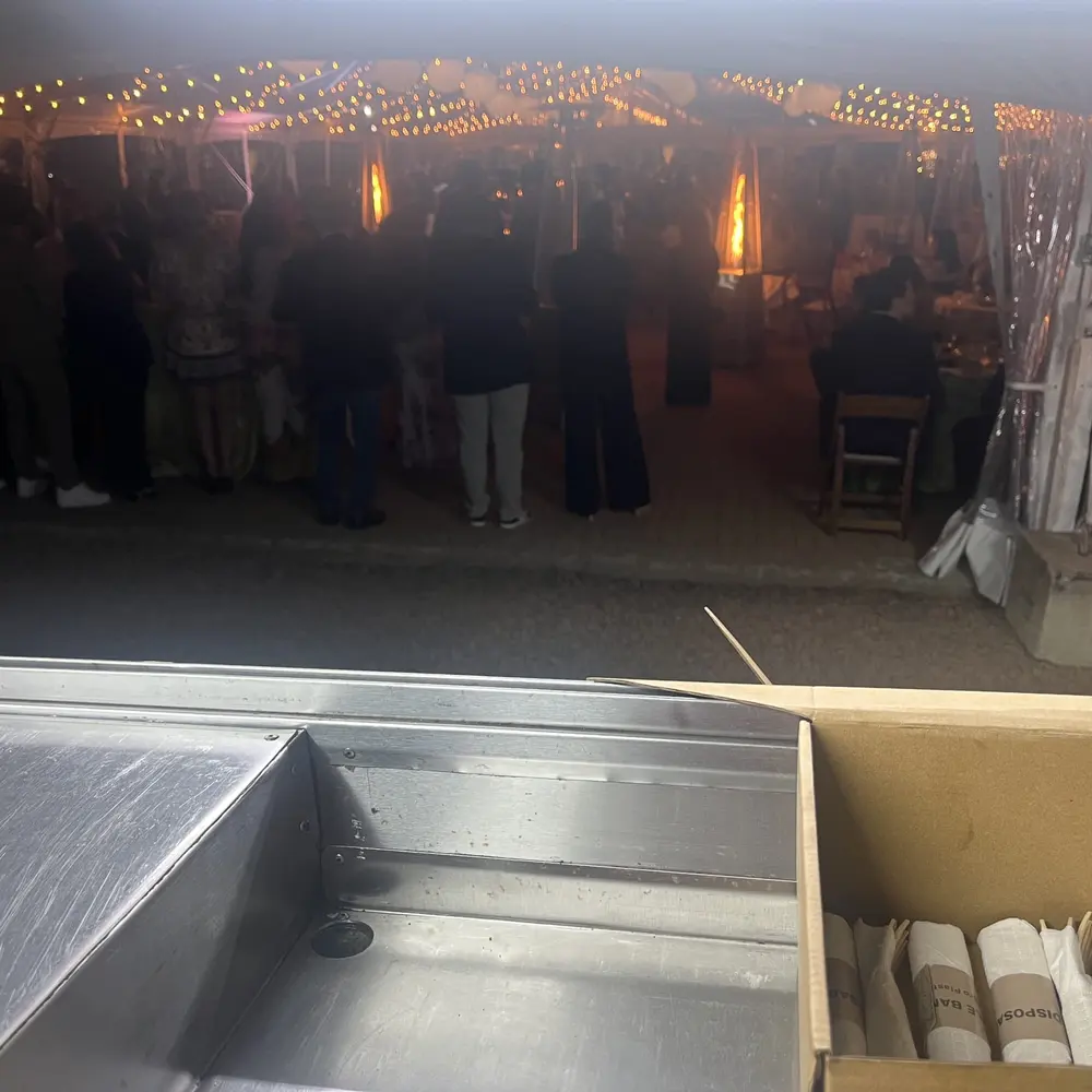 Guests gathered under a string-lit event tent at dusk, seen from the truck's own service window