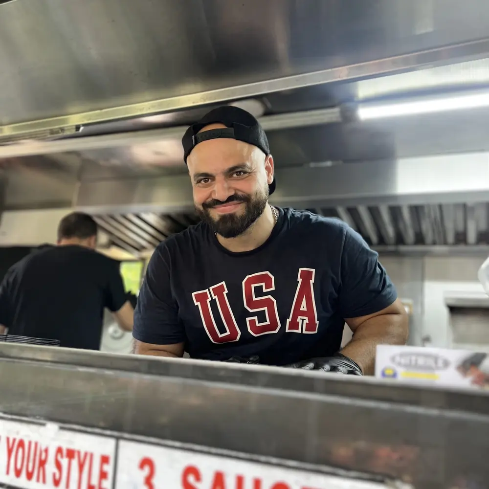 A cook at the order window, with the truck's build-your-own sauce station sign below him