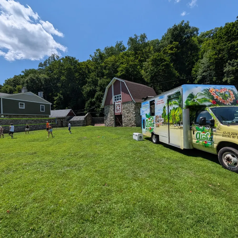 The Aloha truck parked on a wide lawn beside a historic stone-and-timber barn