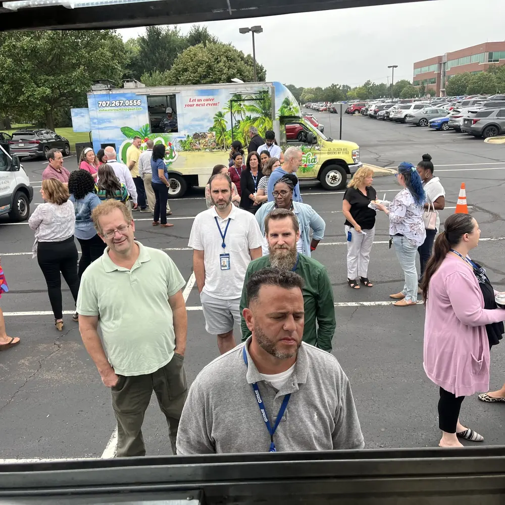 The view out the Aloha truck's order window across a corporate campus where guests are gathering