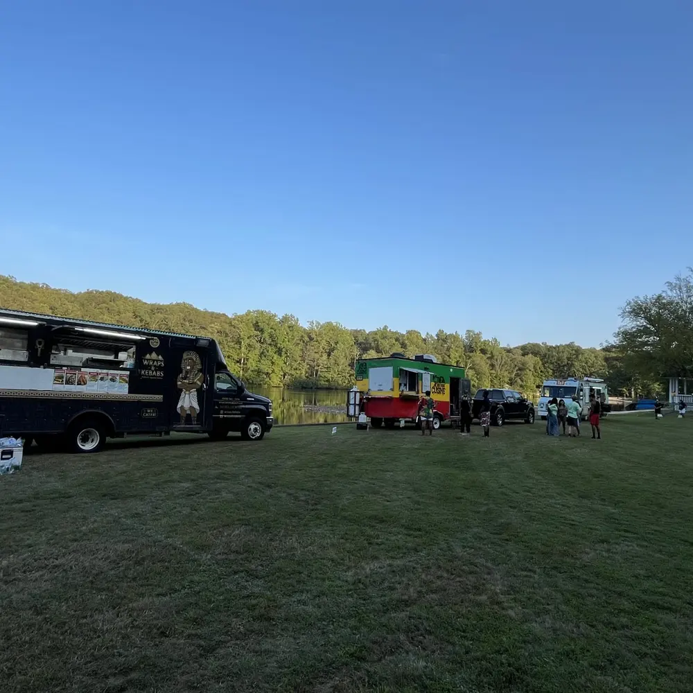 The Wraps & Kebabs truck parked beside a lake at dusk, with other food trucks lined up in the distance