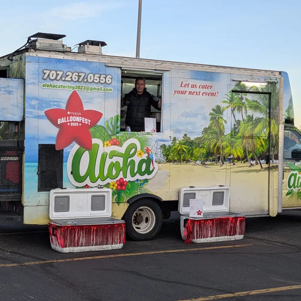 The Aloha truck lit up in the evening at a Balloonfest event, a crew member visible in the window