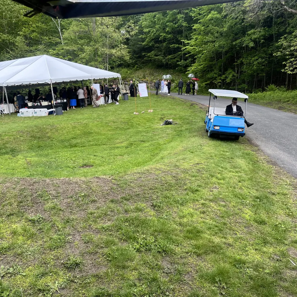 A wide view of the tented event grounds, with a golf cart on the gravel path through the woods
