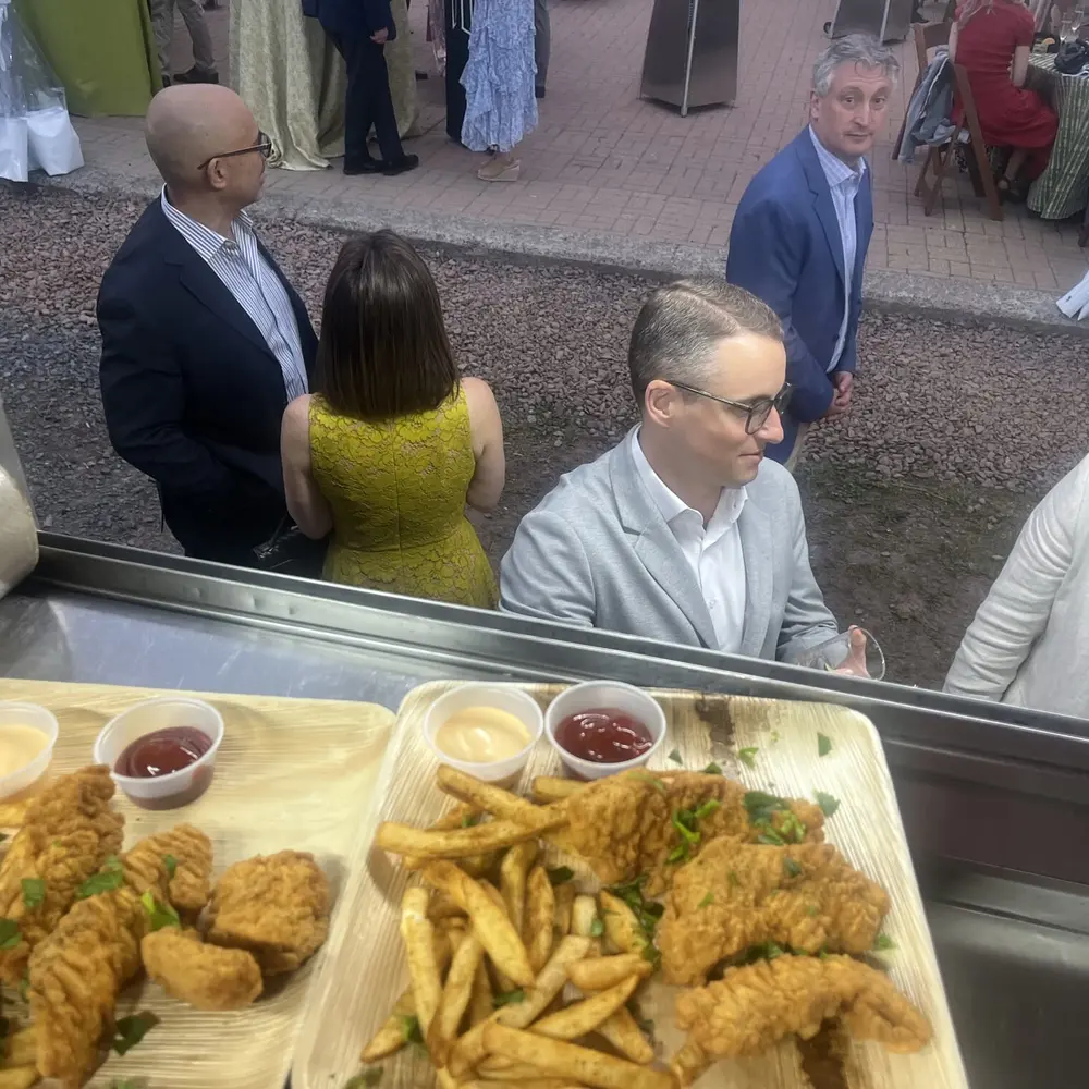 Two trays of fried chicken tenders and fries served through the truck window at an evening event