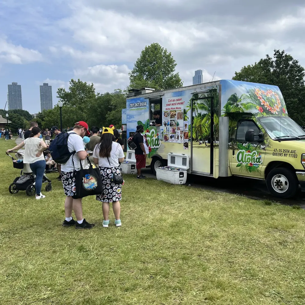 The Aloha truck serving a crowd in a city park with the Manhattan skyline behind it