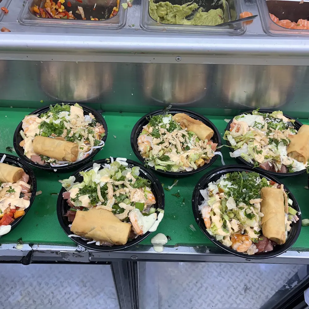 Poke bowls with egg rolls and shredded toppings lined up in the Aloha truck's serving case
