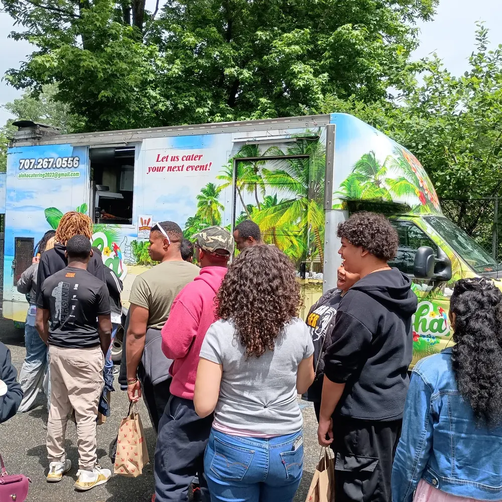 A long line of customers waiting at the Aloha truck in a wooded park