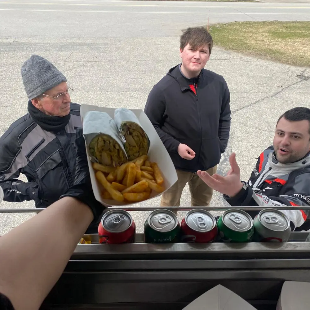 Three motorcycle riders in riding gear holding a tray of wraps and fries at the truck's counter