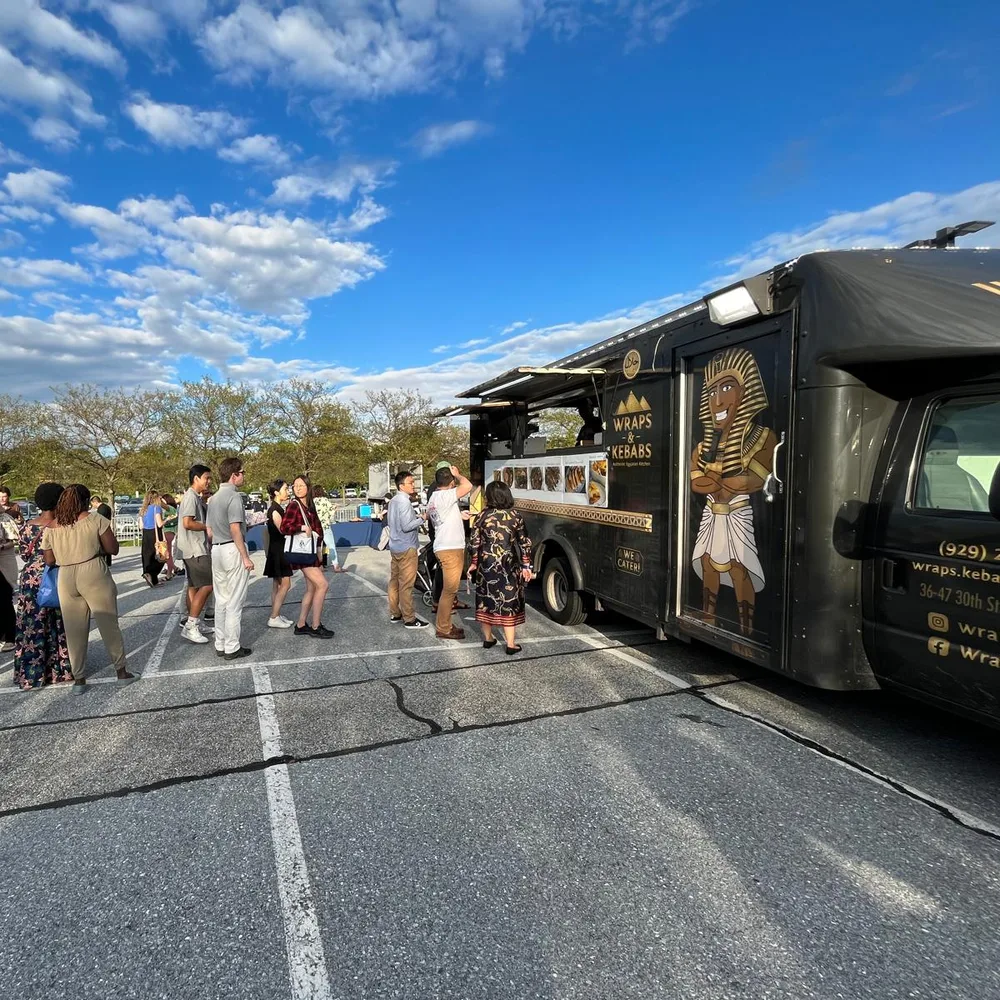 A long line of guests waiting at the Wraps & Kebabs truck under a blue sky