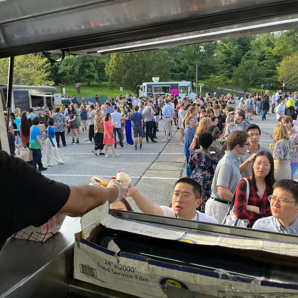 A crew member handing an order out of the truck window to a crowd at a campus event