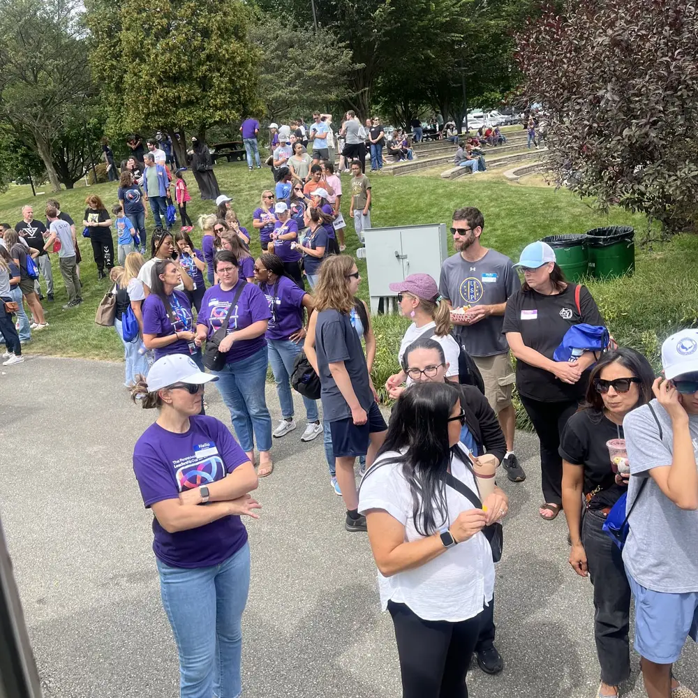 A crowd in purple event T-shirts lined up along a park path, seen from the truck's window